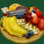 クリスマスタルト18cm.国産イチゴ、バナナのキャラメリゼ、オレンジのロースト、パインの白ワインに、洋梨の赤ワイン煮にサンタ、チョコプレートが載っている