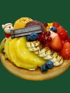 クリスマスタルト18cm．国産イチゴ、バナナのキャラメリゼ、オレンジのロースト、パインの白ワインに、洋梨の赤ワイン煮にサンタ、チョコプレートが載っている
